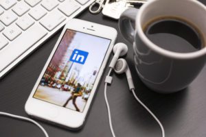 LinkedIn App on iPhone next to coffee and laptop