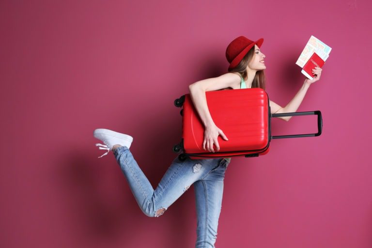 Women posting with luggage on maroon background