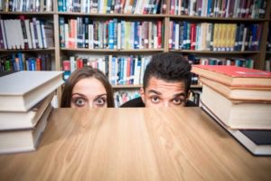 male and female hiding behind table in library